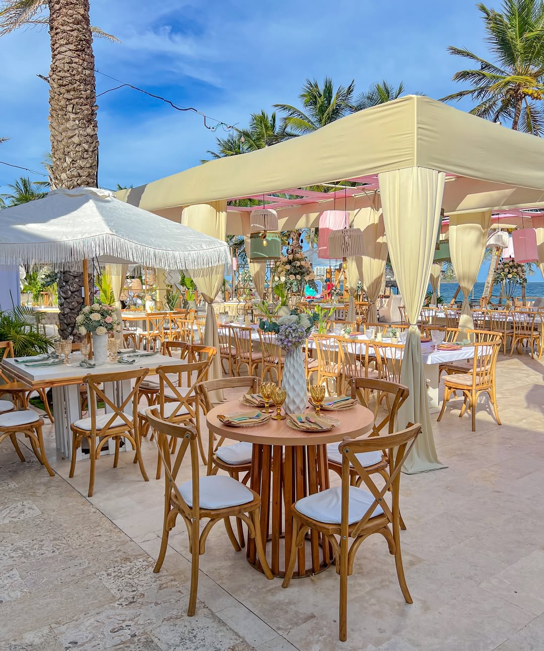 Recepción al aire libre con carpas, lámparas colgantes y mesas en tonos suaves estilo resort